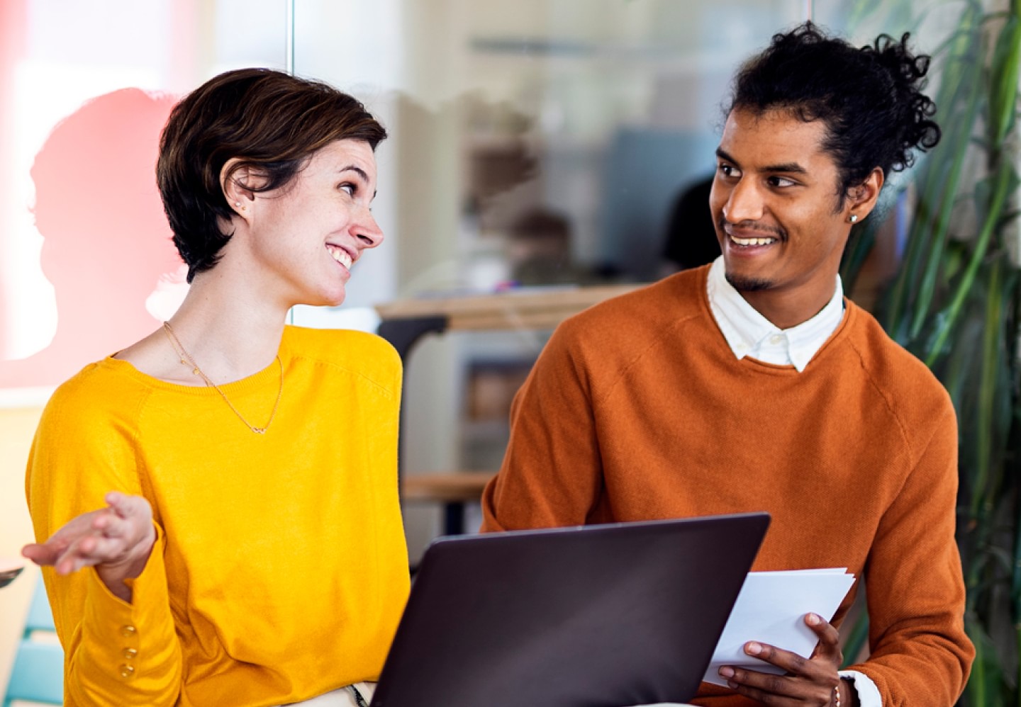 Image of two coworkers chatting in office space with laptop