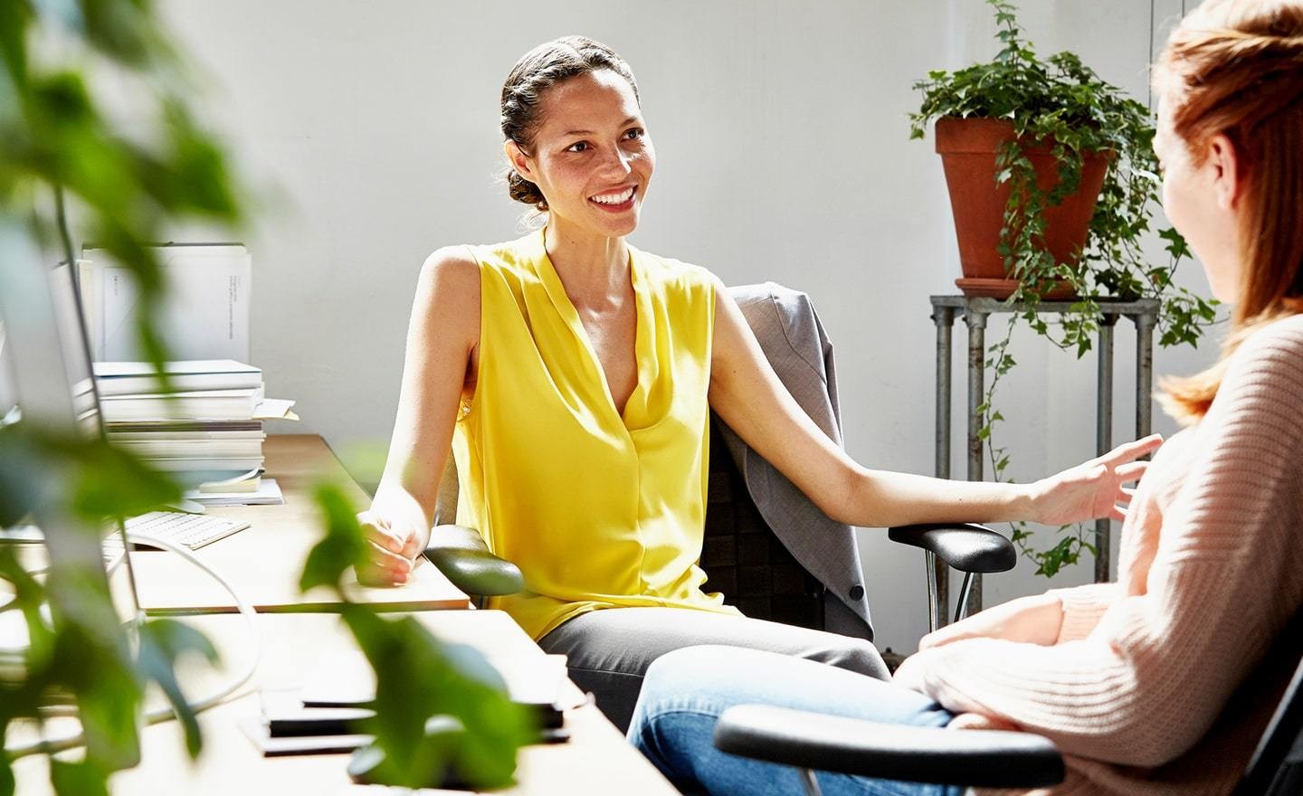 Two women talking in an office with plants