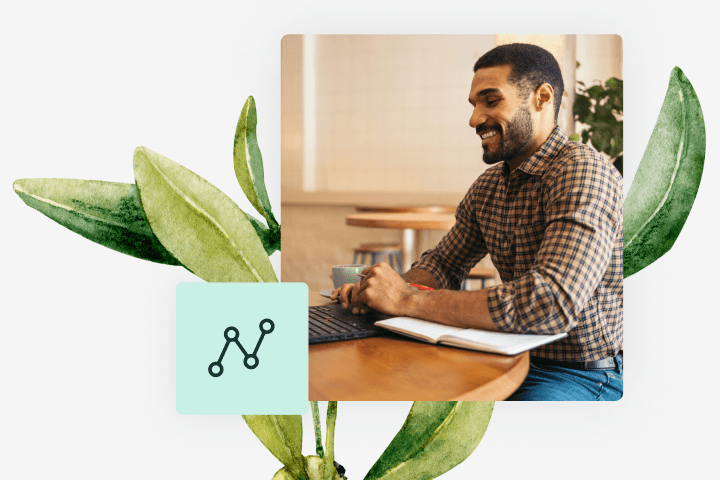 Man sitting on desk while working on laptop with a botanical plant behind