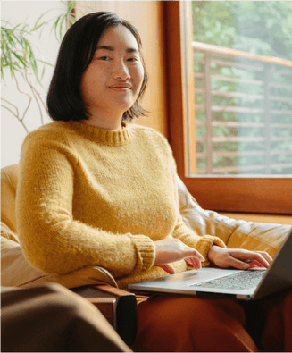 Woman in yellow sweater posing in a warm casual office enviroment with laptop